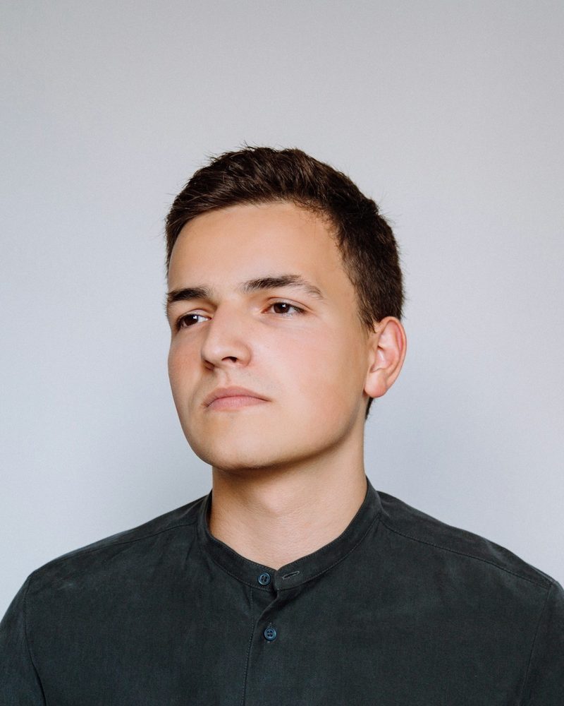 Portrait von Paul mit kurzen dunklen Haaren und dunkelgrünem Hemd vor hellgrauem Hintergrund